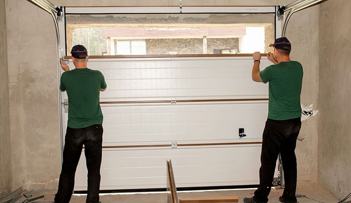 Two technicians installing garage door replacement panel in tracks