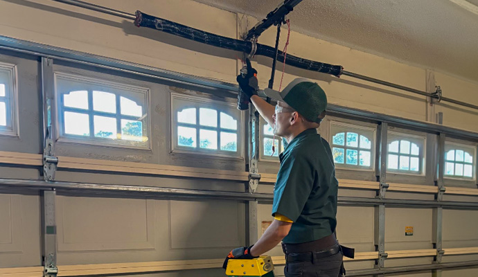 Technician on step ladder lubricating garage door torsion springs