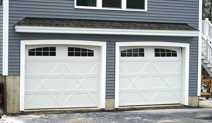 White carriage-style garage doors with arched windows and decorative cross-buck panel inserts on a residential home