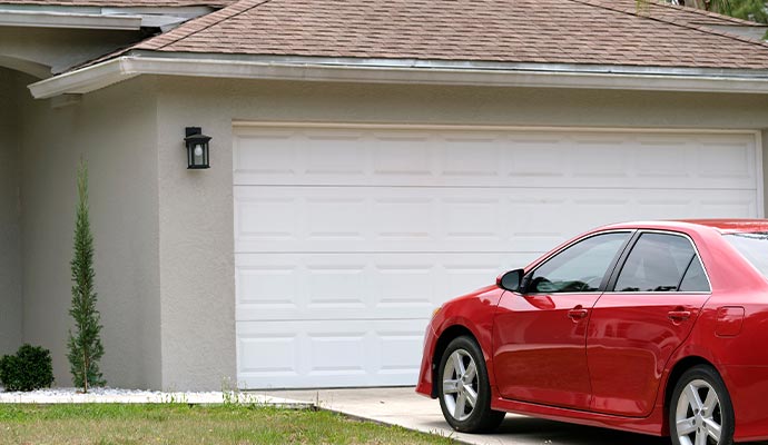 A red car parked in front of a residential garage door